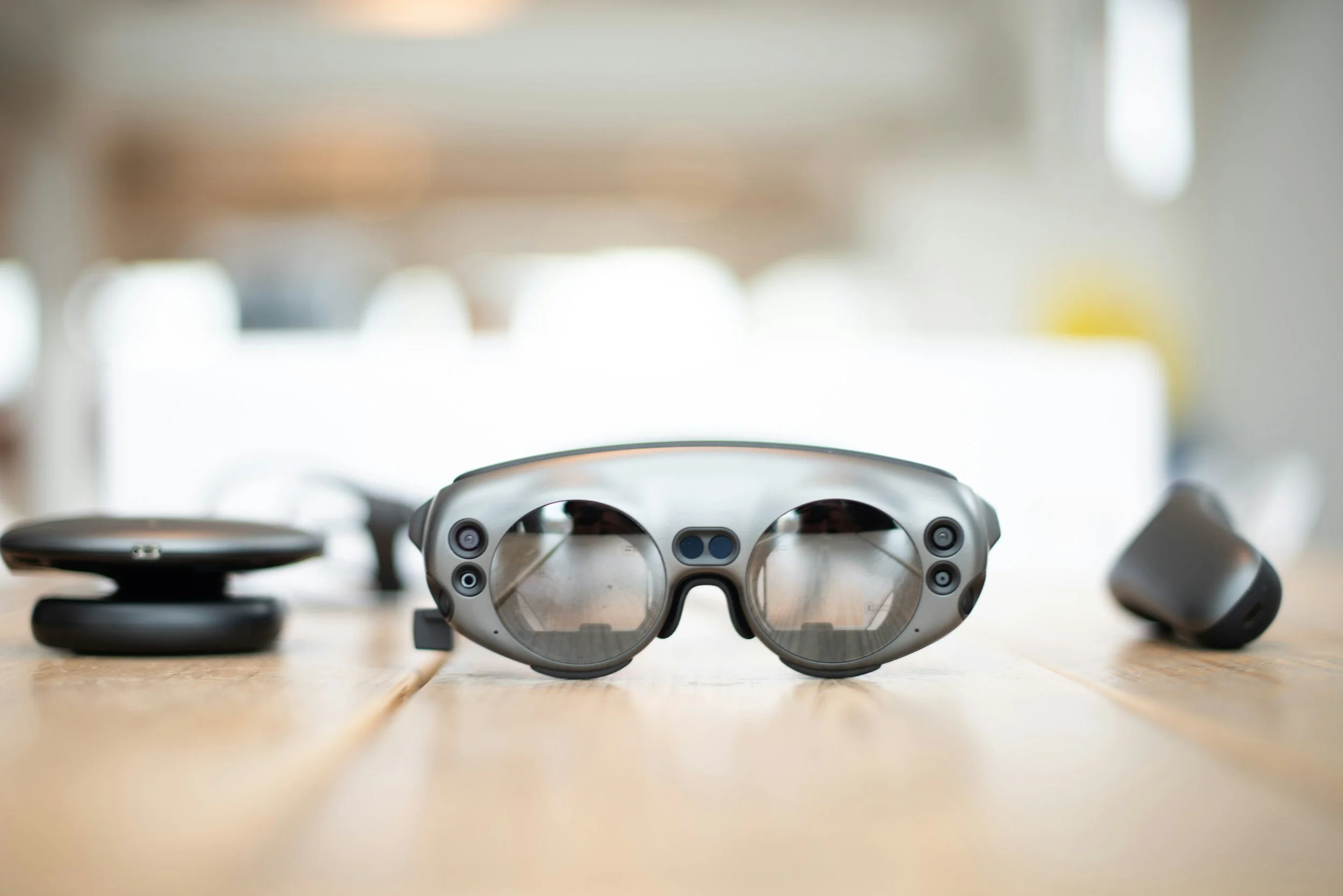 Augmented reality headset on a wooden table, surrounded by accessories in a blurred background.