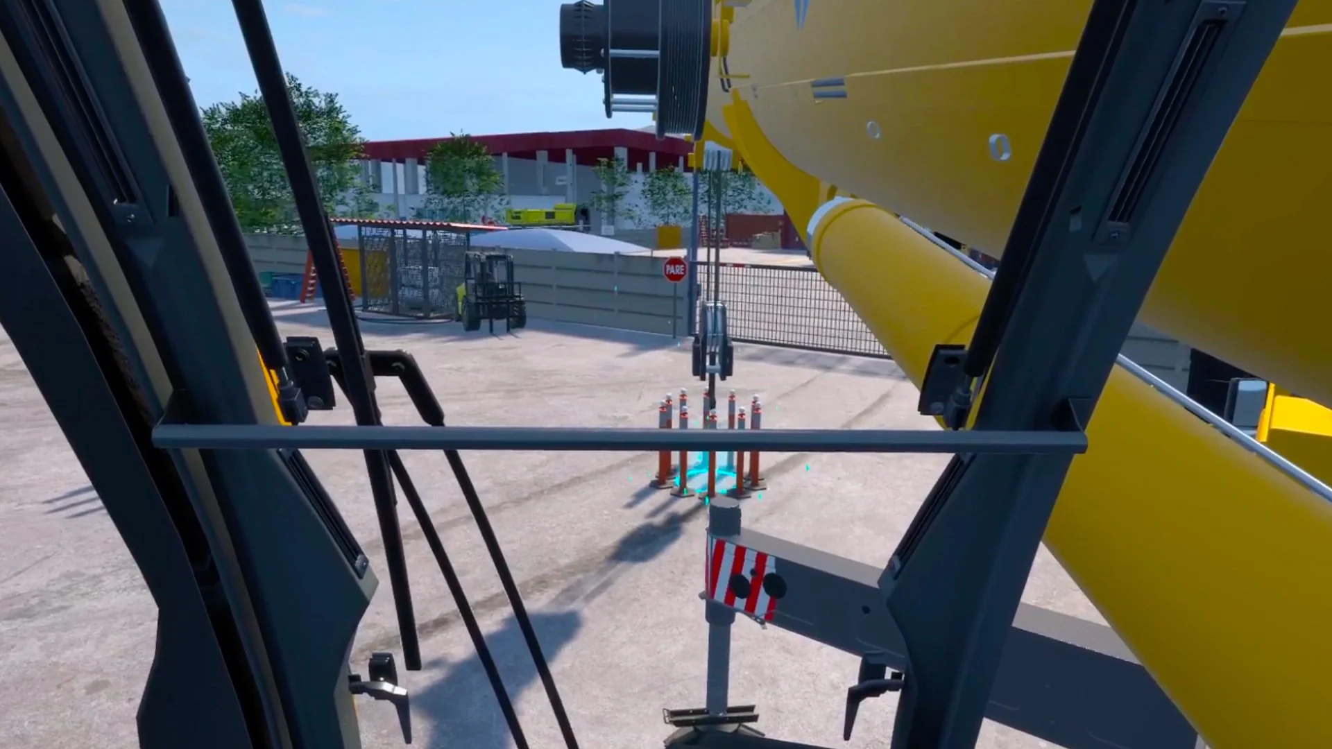 View from inside a crane cab, looking out at a construction site. Visible are the crane's arm, a piece of equipment on the ground, and a forklift in the background. The scene is outdoors, with trees and a building fence in view.