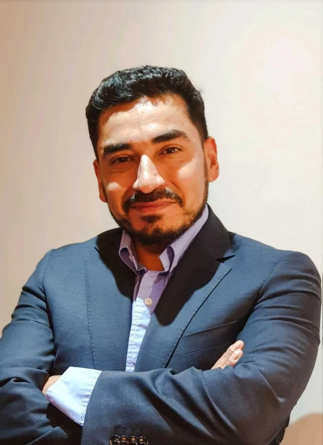 Juan Carlos Muñoz in a suit with arms crossed, smiling.