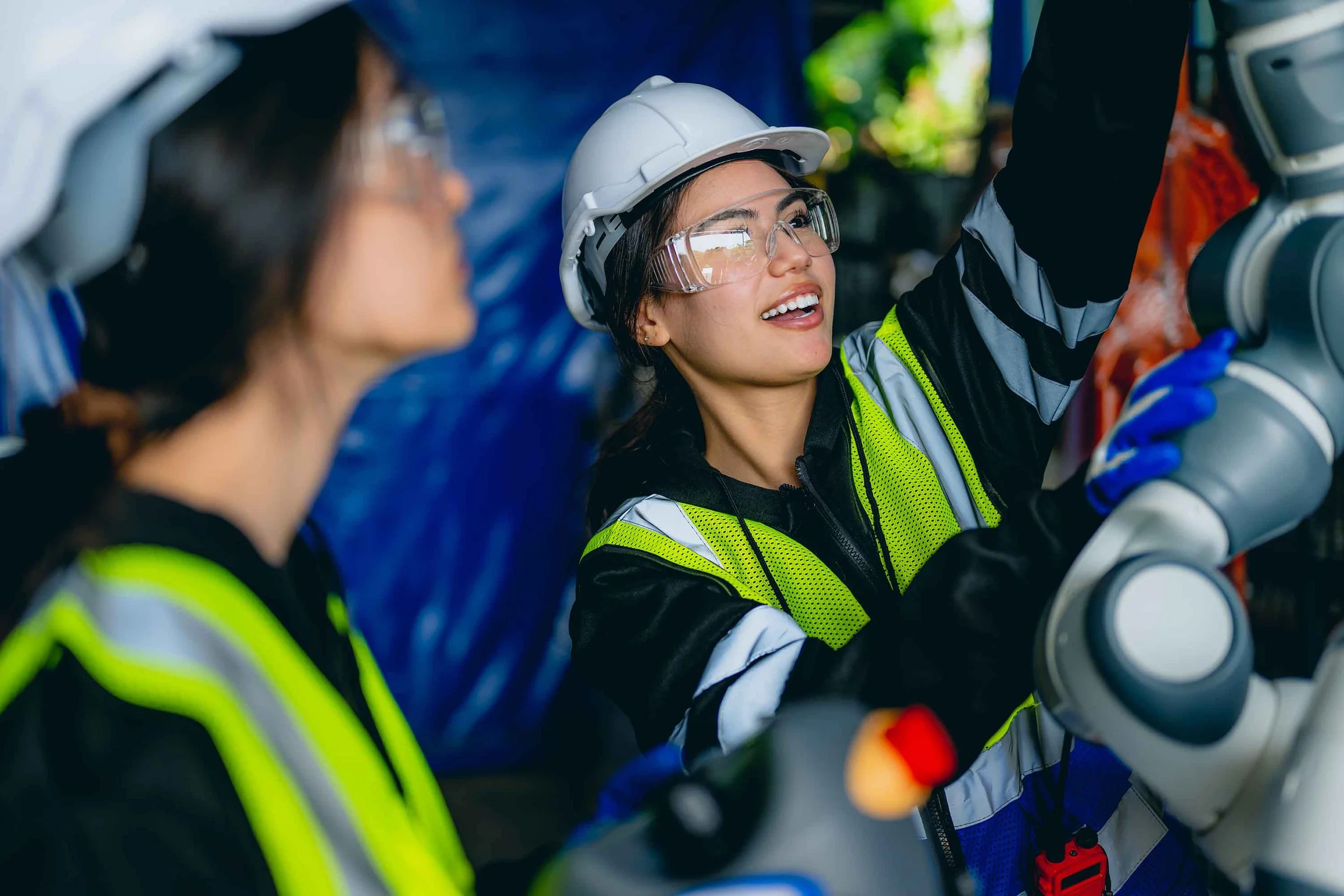 Two female engineers wearing safety gear and hard hats, working with industrial equipment.