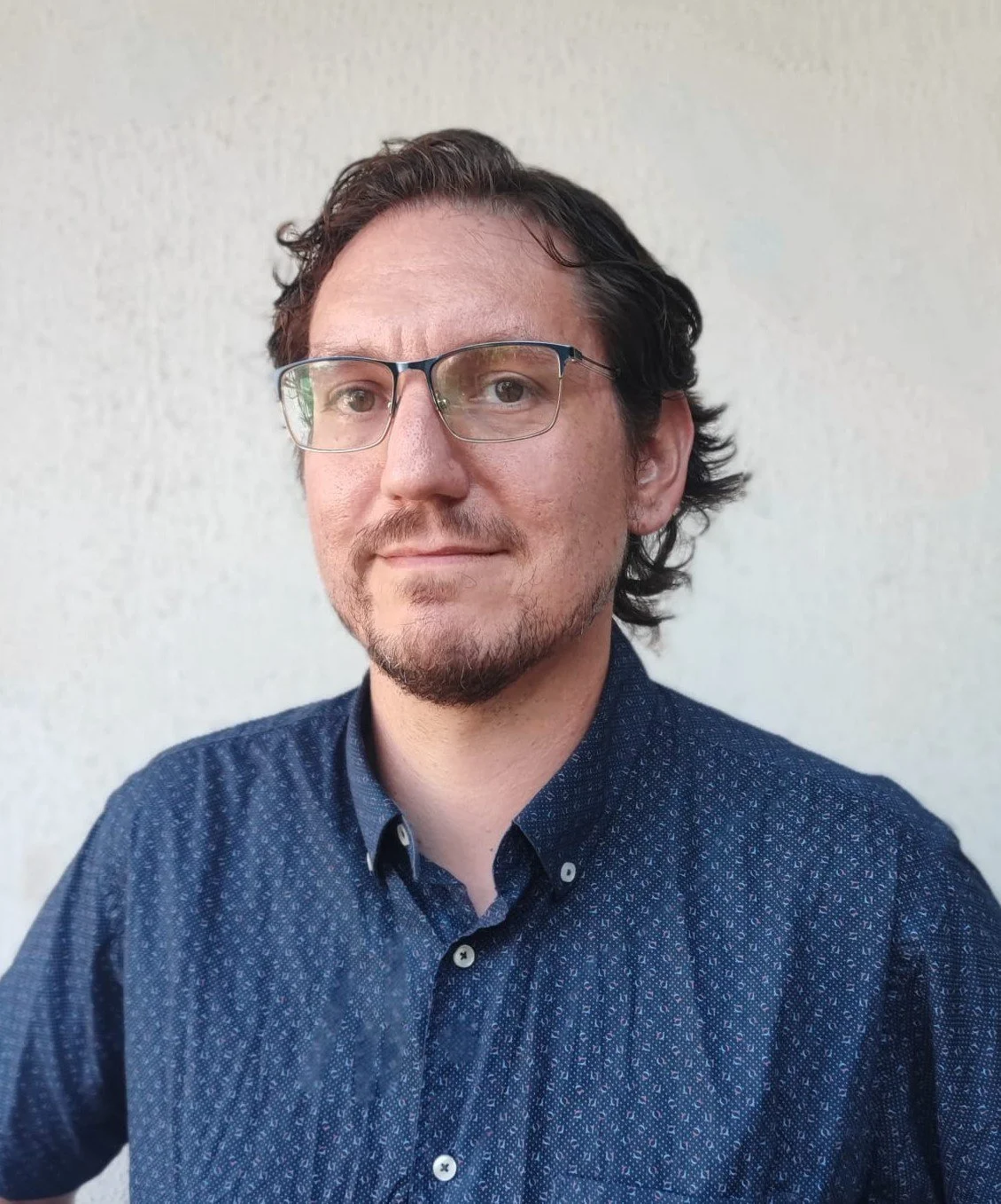 Sergio Silva wearing glasses and a dark blue patterned shirt standing against a plain background.