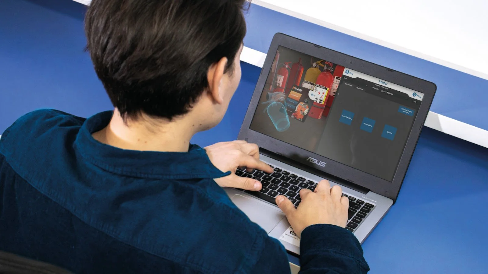 Person using a laptop with a virtual reality simulation displayed on the screen, involving fire extinguishers and safety training.