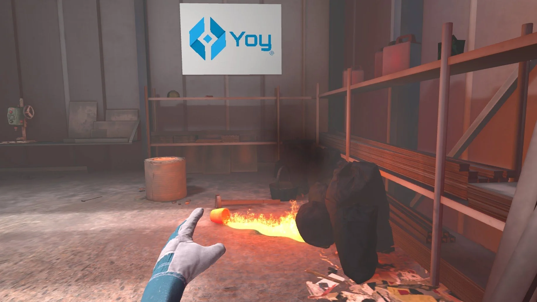A virtual reality game scene depicting a white-gloved hand pointing towards a spilled bucket with flames. The setting appears to be an industrial storage room with shelves holding various items. A sign with a blue logo and the word 'Yoy' is mounted on the wall.