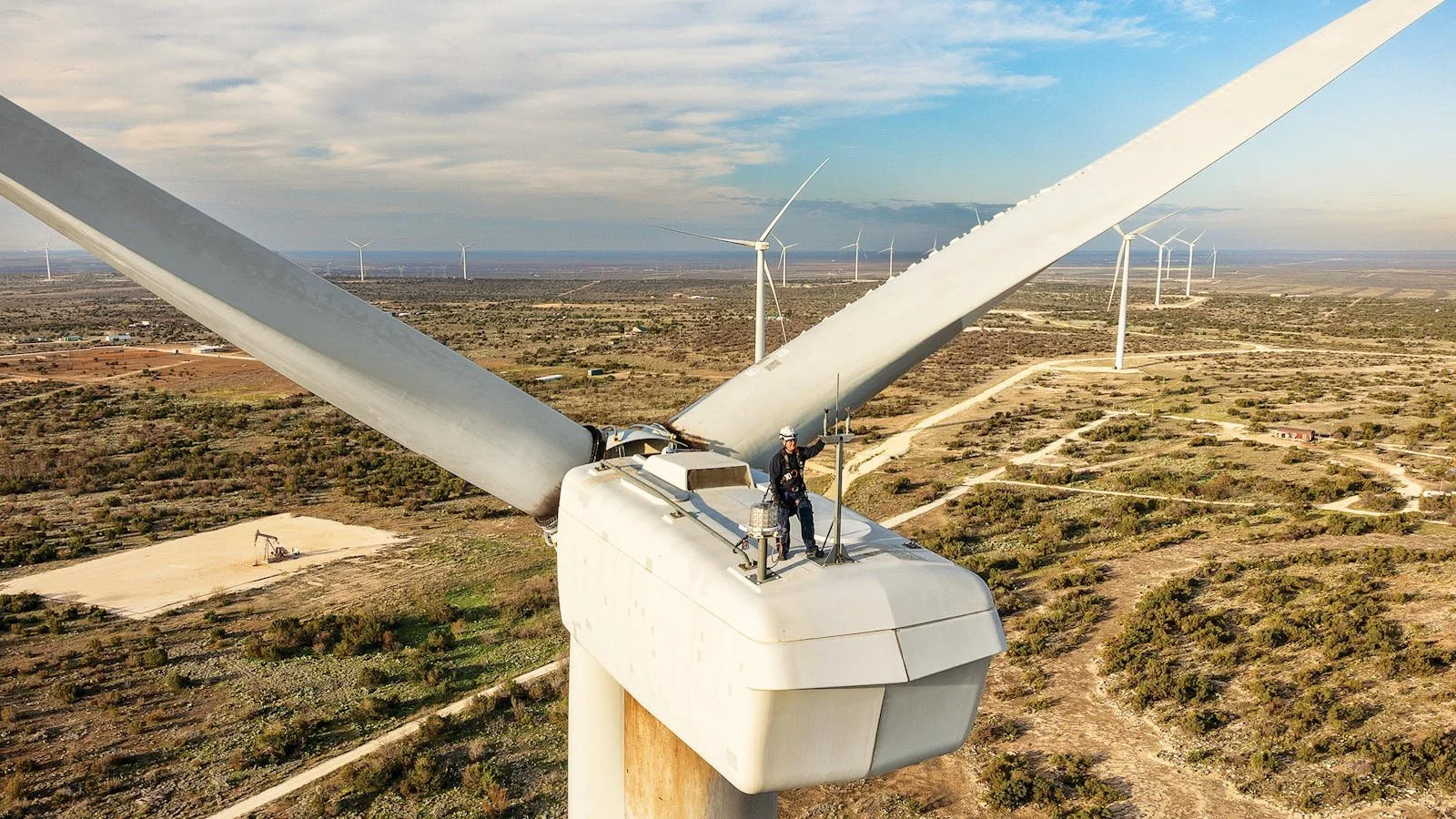 Wind turbine maintenance worker on rotor in a wind farm landscape.