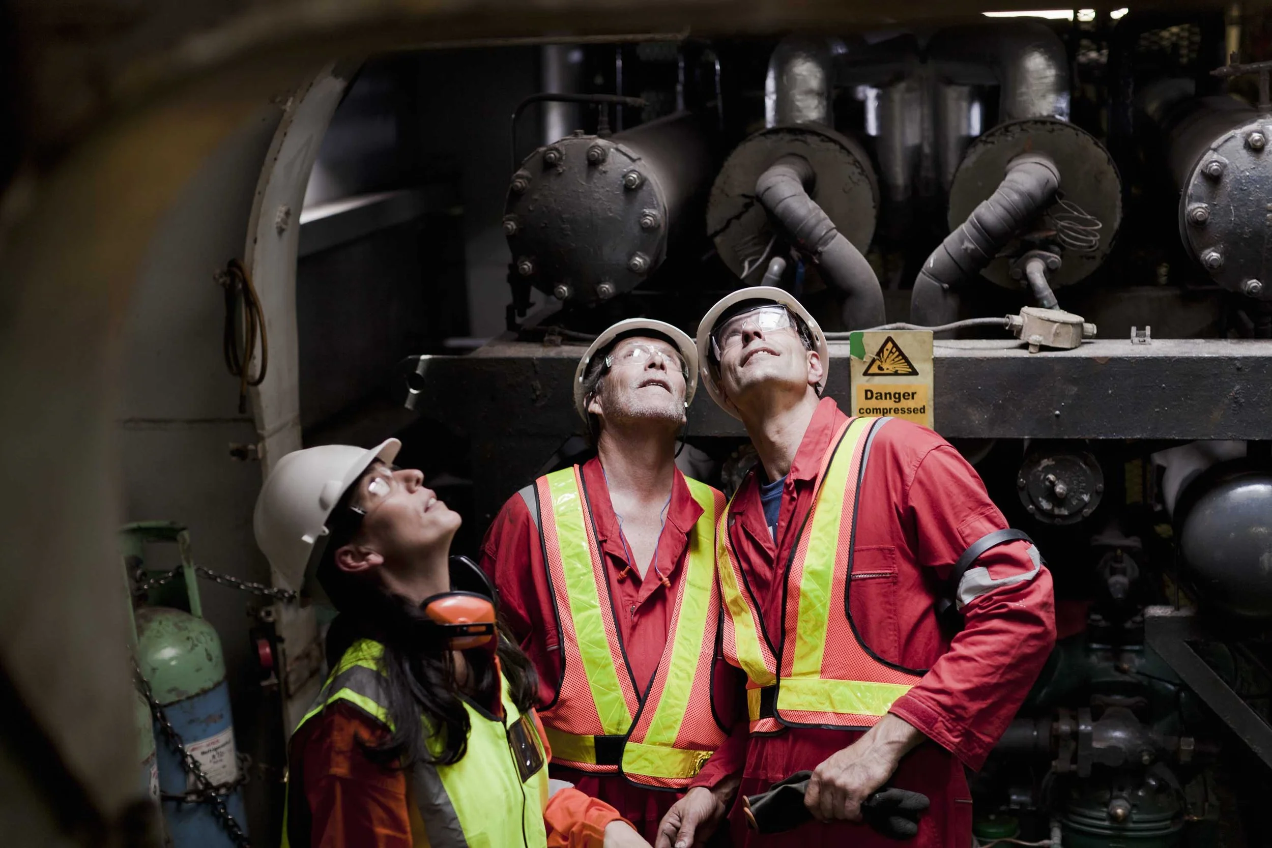 Three industrial workers in safety gear inspecting machinery.