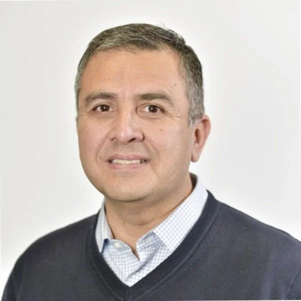 Portrait of a man in a dark sweater and collared shirt against a plain background.