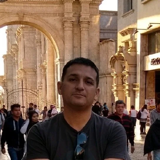 Man standing in front of an ornate stone archway on a busy street.